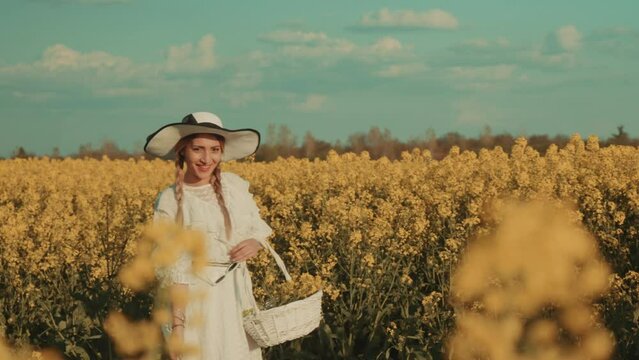 Beautiful young woman in white dress on yellow flower meadow in sunset