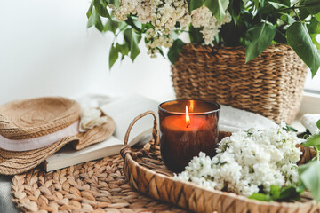 Burning candle and basket of white lilacs in home interior