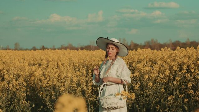 Beautiful young woman in white dress on yellow flower meadow in sunset