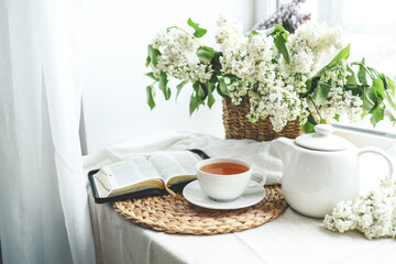 A cup of tea, a basket of lilacs and an open Bible