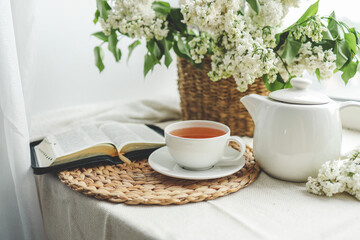 A cup of tea, a basket of lilacs and an open Bible