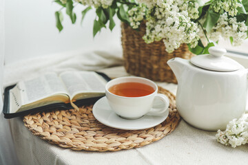 Fototapeta na wymiar A cup of tea, a basket of lilacs and an open Bible