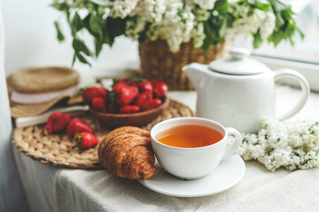 Cup of tea, croissant, strawberry and lilac basket, summer morning aesthetic