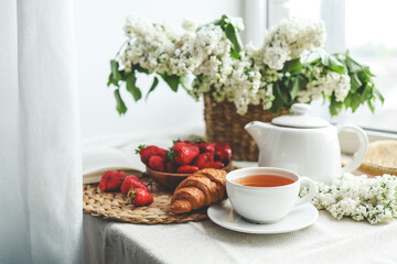Cup of tea, croissant, strawberry and lilac basket, summer morning aesthetic
