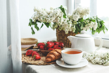 Cup of tea, croissant, strawberry and lilac basket, summer morning aesthetic