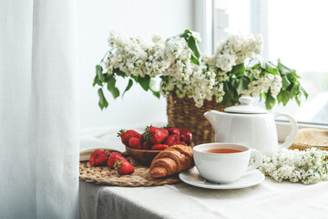 Cup of tea, croissant, strawberry and lilac basket, summer morning aesthetic