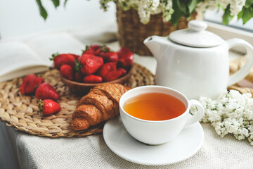 Cup of tea, croissant, strawberry and lilac basket, summer morning aesthetic