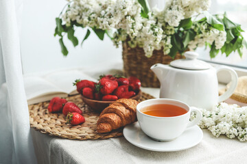 Cup of tea, croissant, strawberry and lilac basket, summer morning aesthetic