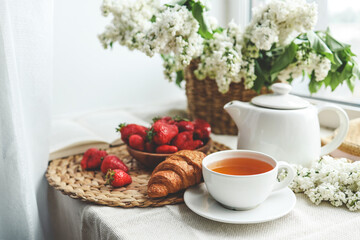 Cup of tea, croissant, strawberry and lilac basket, summer morning aesthetic