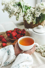 Cup of tea in hands, strawberries and flowers, summer breakfast concept