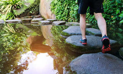 Young man walking crossing a river on stones