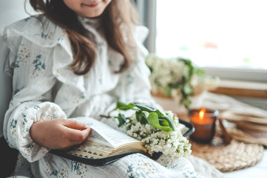 Girl reading the Bible, open book and lilac branch, cozy photo
