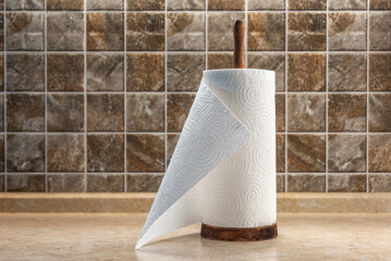 Paper towels on a wooden holder on the table against the background of a tiled wall. Selective focus.