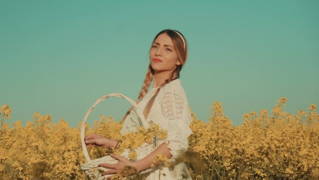 Beautiful young woman in white dress on yellow flower meadow in sunset