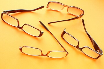 Old broken eyeglasses with damaged legs on orange background. Poor eyesight. Reuse and repair...