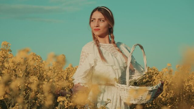 Beautiful young woman in white dress on yellow flower meadow in sunset