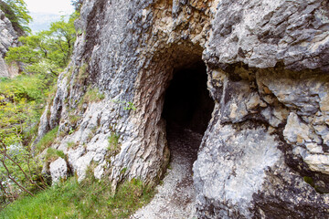 Rock wall with a dark hole, entrance to the cave in Jura mountains, hiking trail, Gorges de Court,...