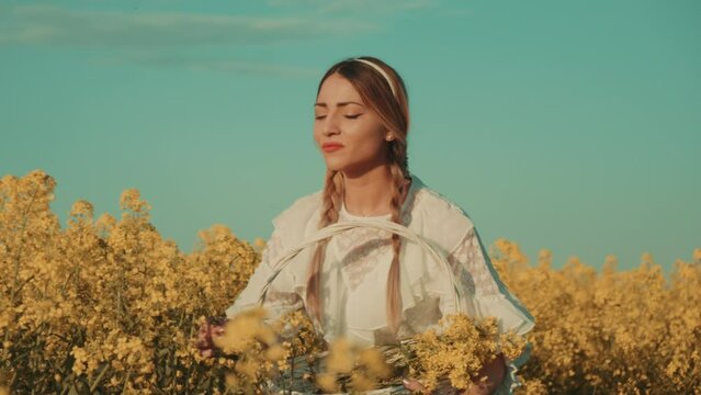 Beautiful young woman in white dress on yellow flower meadow in sunset