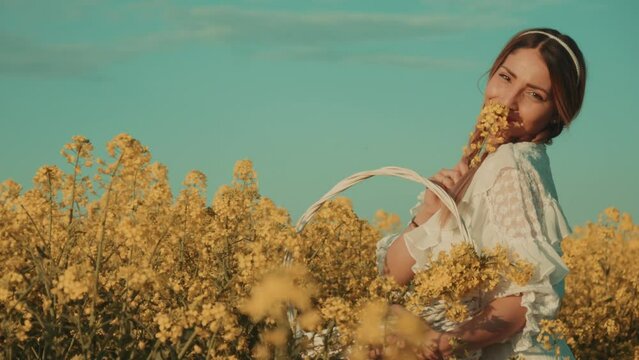 Beautiful young woman in white dress on yellow flower meadow in sunset