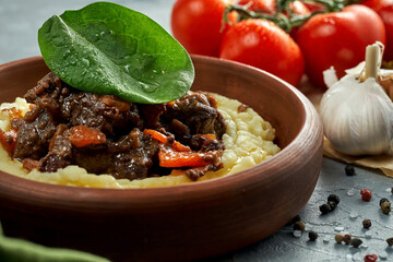 Mashed potatoes with stewed meat in a clay dish on a concrete background