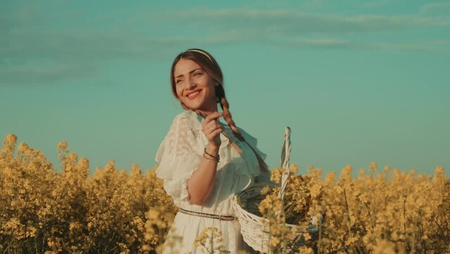 Beautiful young woman in white dress on yellow flower meadow in sunset
