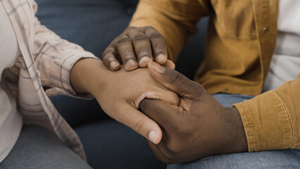 Close-up of African American man tenderly stroking hands of his wife, comforting and supporting her