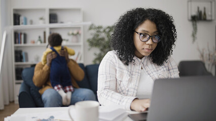 Father sitting with a baby while mother is working on laptop, parental leave