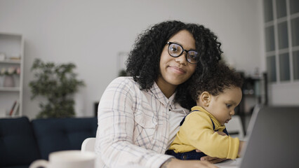 Portrait of successful African American woman working on laptop and taking care of her baby