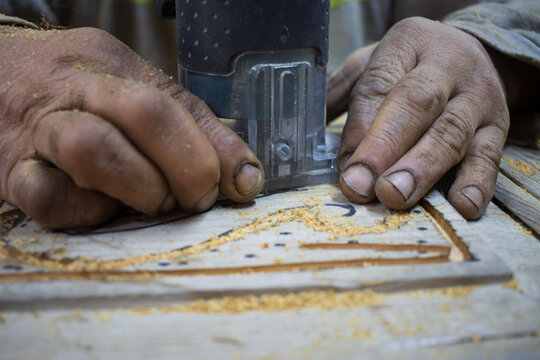 Close Up of Man Hands carving on wooden furniture. Carpenter using tool making Artistic Wood Carving. Producing an Ornament on Wood with Chisel and Hammer on a Panel of Wood . High quality photo