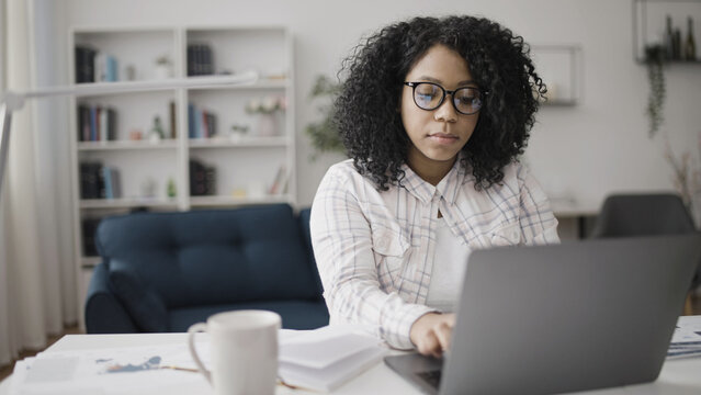 An African American woman freelancer typing on her laptop while sitting in her cozy home office