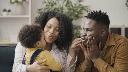 Happy mother and father making faces to cheer up their crying toddler, parenting