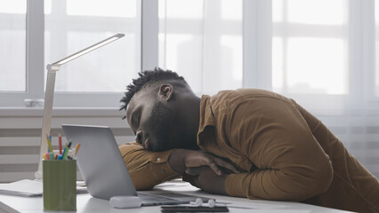 Overworked African American man sleeping in front of laptop, work fatigue, freelance