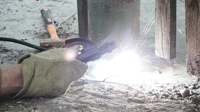Welding of metal. The welder brews a gap in the pipe serving as a fence post using electrode welding. Siberia.