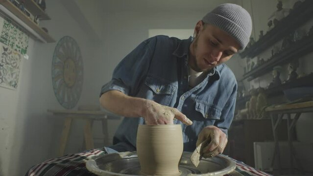 The potter adds unique lines to the blank on the potter's wheel. A beautiful background of the workshop behind the artist. High quality 4k footage