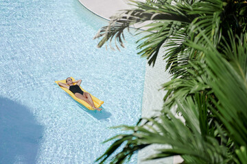 Enjoying suntan. Tropical vacation concept. Top view of young woman on the yellow air mattress in...