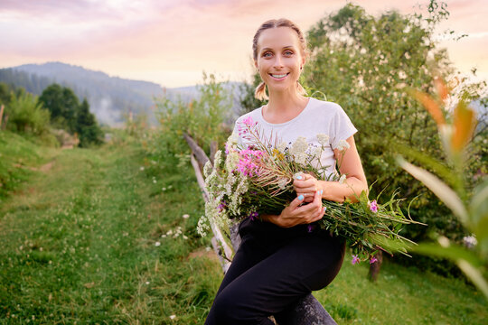 Outdoor portrait of Happy young woman holding bouquet of herbal and wild flowers.