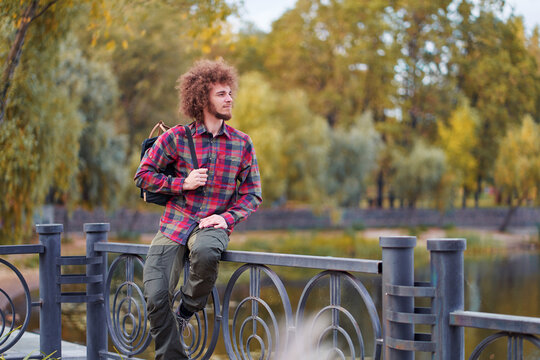 Outdoors portrait of young man with curly hair in the park on the river promenade.