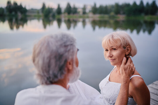 Romantic holiday. Senior loving couple sitting together on lake bank.