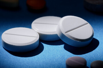 Pharmacy health care and drugs concept. Macro of three white tablets among different kinds of pills on blue background.