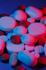 Extasy and drug concept. Close up shot of white and colored pills of different kind lit with red and blue neon lights.