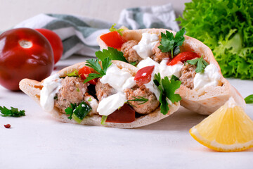 Pita pocket stuffed with meatballs and vegetables topped with sour cream and cilantro. Arabian, Turkish and Greek cuisines meal