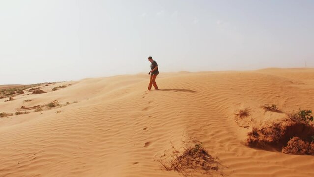 Young man runs barefoot on sandy hill in desert and looks back. Concept of choice and doubt. Slow motion
