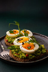 Sandwiches with rye bread and guacamole, with boiled eggs and microgreens of peas and radishes and sesame seeds, a plate with sandwiches close-up on a green background