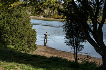 Fototapeta na wymiar Young man seen between trees practices sport fly fishing in the Rio Grande or Futaleufú River, in Chubut, Patagonia Argentina.