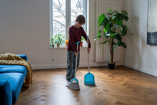 Household chores for children. Schoolboy child sweeping floor. Kid boy holding broom and shovel helping to clean house, learning how to sweep while cleaning his room at home