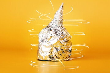 Hat made of aluminium foil on yellow background. Afraid of 5G radiation or aliens. Symbol for conspiracy theory