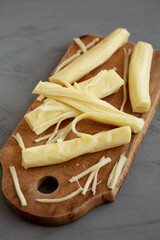 Organic String Cheese on a rustic wooden board on a gray background, side view.