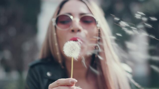 Attractive smiling woman blowing dandelion