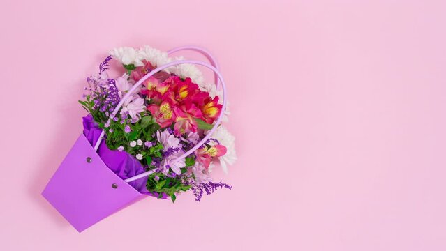 Bouquet of natural flowers in a purple bag appears on a pink background. Greeting card for birthday, mother's day, women's day or other occasion. Stop motion animation. Copy space. Flat Lay.