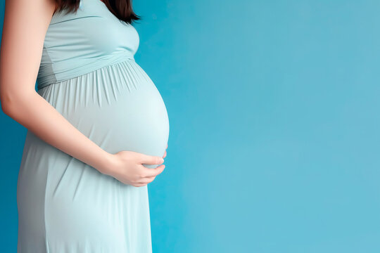 A pregnant caucasian woman in blue dress strokes her belly on blue background. Place for text. Copy space. Waiting for the birth of a child. High quality photo